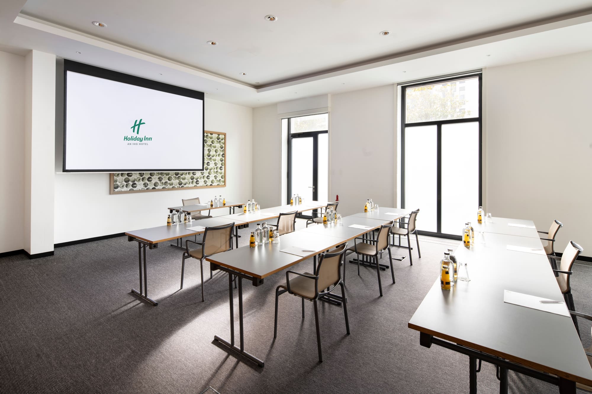 Ein Tageslicht-Tagungsraum im Holiday Inn Frankfurt - Alte Oper mit fest installierter Leinwand und Projektor, bis zu 90 Personen in Reihenbestuhlung.